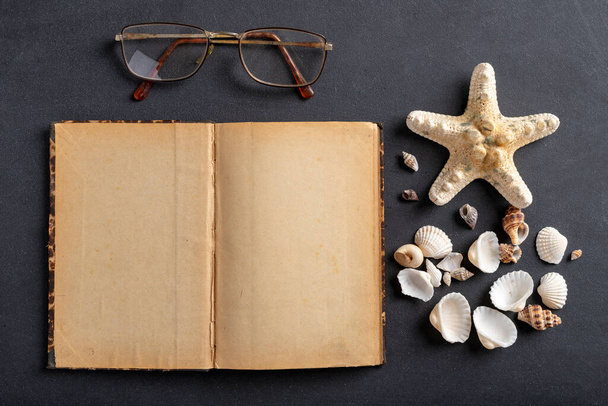 Old yellowed notebook, glasses and seashells. A place to save your holiday memories. Dark background. - Foto, immagini