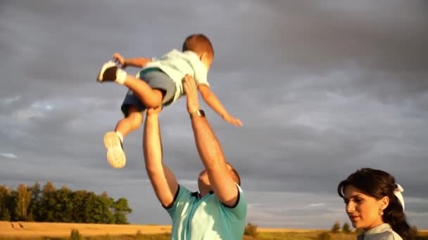 Een man die met z 'n vrouw op het veld staat, kotst z' n zoon in traag tempo in de lucht. - Video