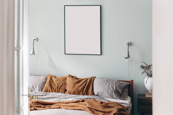 Portrait black picture frame mockup on sage green wall. Bedroom view through open white door. Grey linen and rusty muslin pillows on wooden bed. Scandinavian interior. Ceramic vase with dry grass. - Фото, зображення
