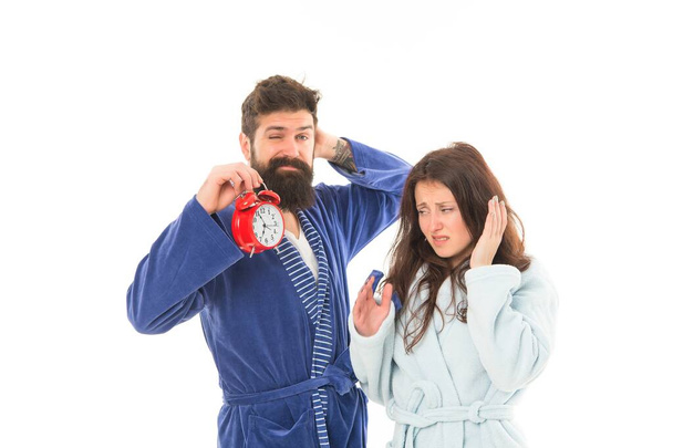 A sleepy morning. Couple in love waking up in morning. Pretty woman and bearded man holding alarm clock early in the morning. Sexy girlfriend and brutal hipster wearing nightrobes in morning - Φωτογραφία, εικόνα