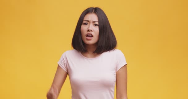 Enojada mujer asiática señalando con el dedo a la cámara, sospechando y culpando en la mentira, fondo naranja - Imágenes, Vídeo