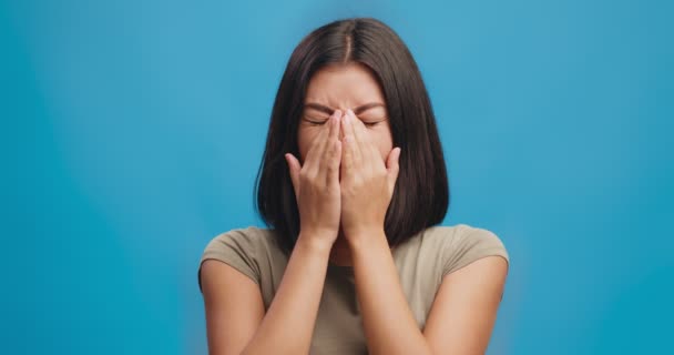 Gezichtsproblemen. Jonge aziatische dame die oogpijn voelt, neusbrug masseren, oogspanning, blauwe studioachtergrond - Video