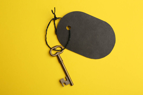 Винтажный ключ с пустым тегом на желтом фоне, вид сверху. Ключевые слова - Фото, изображение