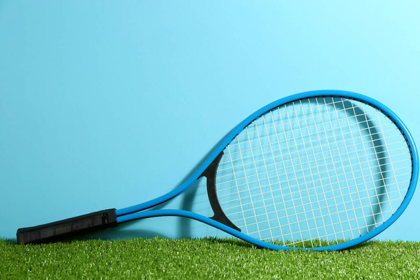Tennis racket on on green grass against light blue background. Space for text - Zdjęcie, obraz