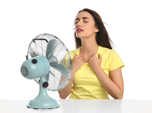 Woman suffering from heat in front of fan on white background. Summer season - Фото, изображение