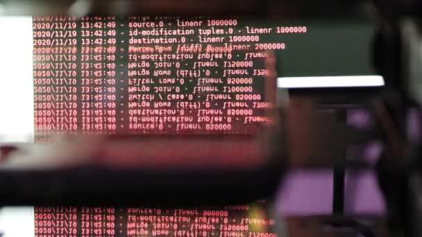 Kód softwaru červeného počítače pohybující se na černém monitoru se odráží na skle. Abstraktní hackování počítače v procesu se základnou rack serveru, dynamický text běží a teče na obrazovce PC. - Záběry, video