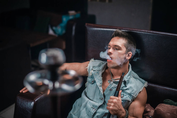 Мужчина курит ароматный восточный кальян в шланге шиши. - Фото, изображение