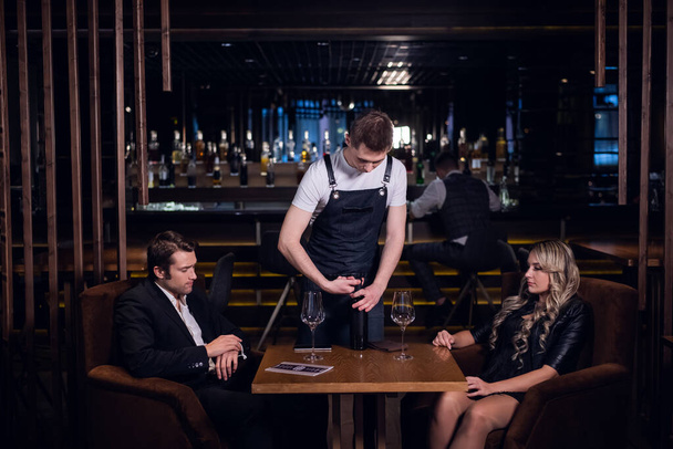 un joven camarero abre una botella de vino en la mesa de un restaurante - Foto, imagen