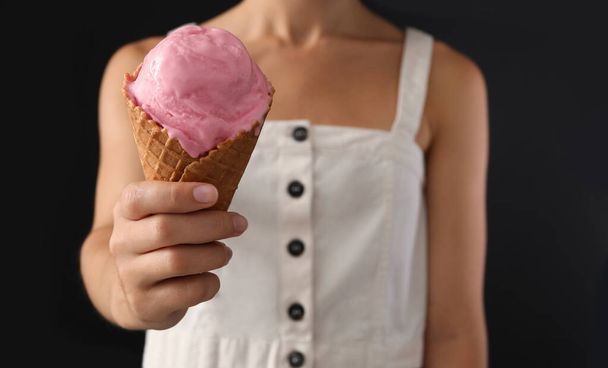 Woman holding pink ice cream in wafer cone on black background, closeup - Фото, зображення