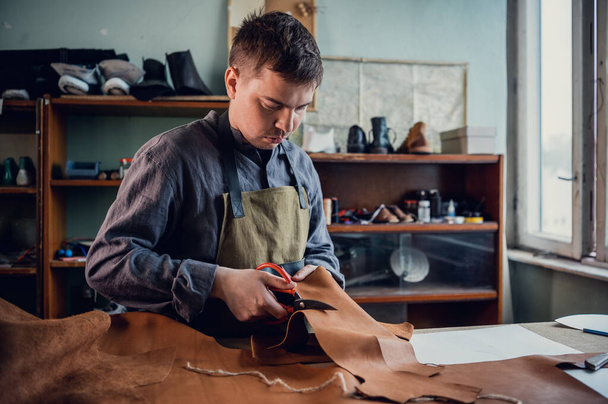 En la clase magistral para la producción de zapatos, un zapatero experimentado corta el cuero con tijeras - Foto, Imagen