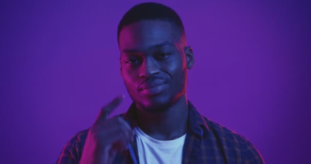 Hombre afroamericano guapo apuntando a su cabeza, haciendo gestos piense usted mismo, estudio filmado con luces de neón, de cerca - Metraje, vídeo