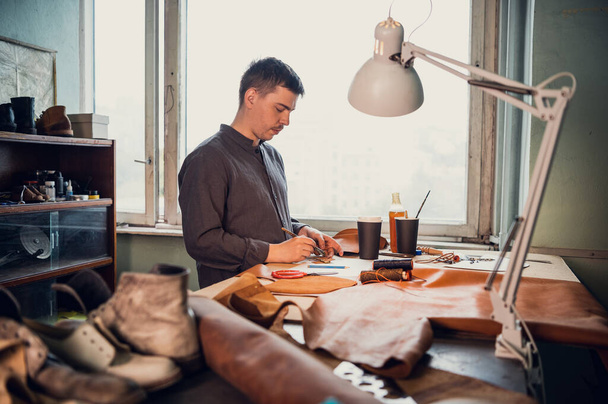 A young old-school shoemaker fulfills an order to make an exclusive leather product. Portrait in the studio - 写真・画像