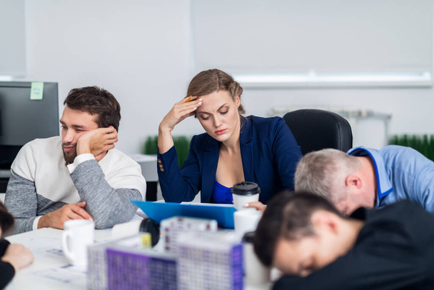 Business people sleeping in the conference room during a meeting, while their colleague is trying to concentrate on the documents she is studying - Foto, Bild