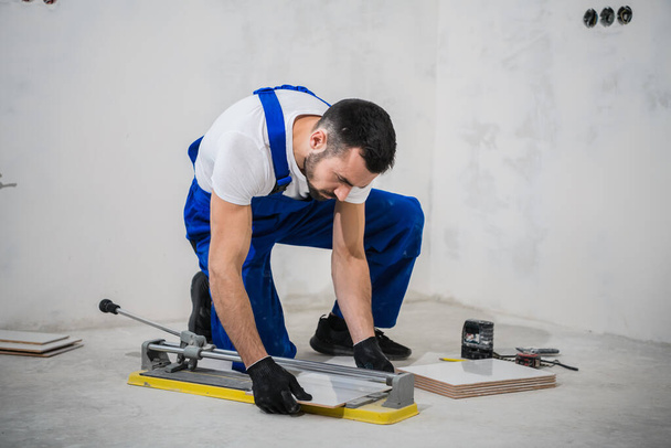Trabalhador em roupas de trabalho azul usa um cortador de telhas - Foto, Imagem