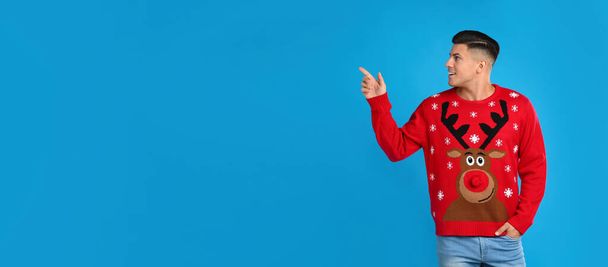 Handsome man in Christmas sweater pointing on blue background, space for text - Фото, зображення