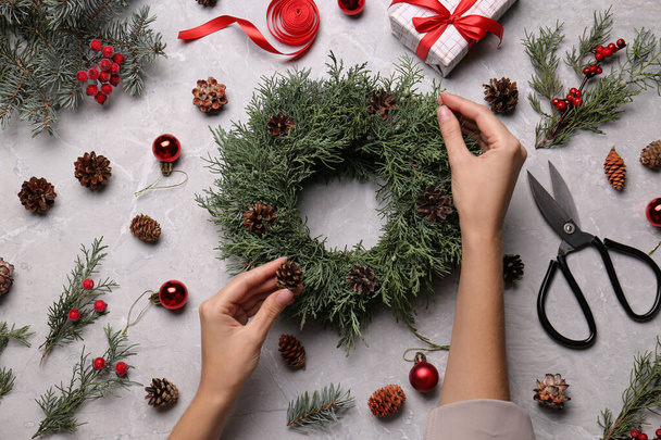 Florist making beautiful Christmas wreath with pine cones at grey table, top view - 写真・画像