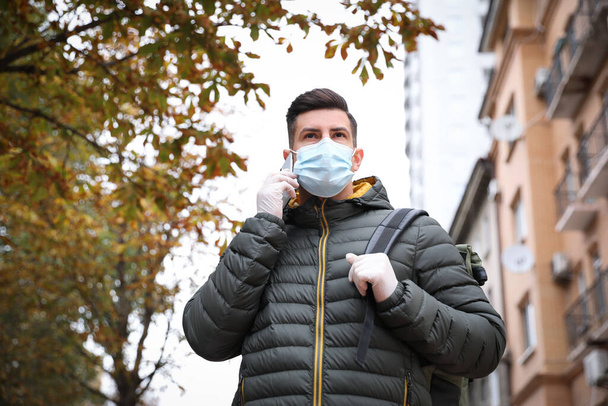 Man in medical face mask and gloves talking on phone while walking outdoors. Personal protection during COVID-19 pandemic - Photo, image