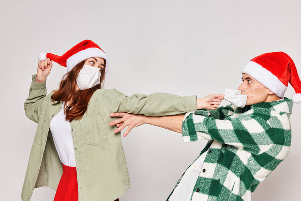 Noel Baba şapkalı genç çift stüdyonun gri arka planında eğleniyor. - Fotoğraf, Görsel