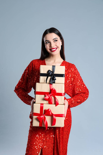 Woman in red dress holding Christmas gifts on grey background - Φωτογραφία, εικόνα