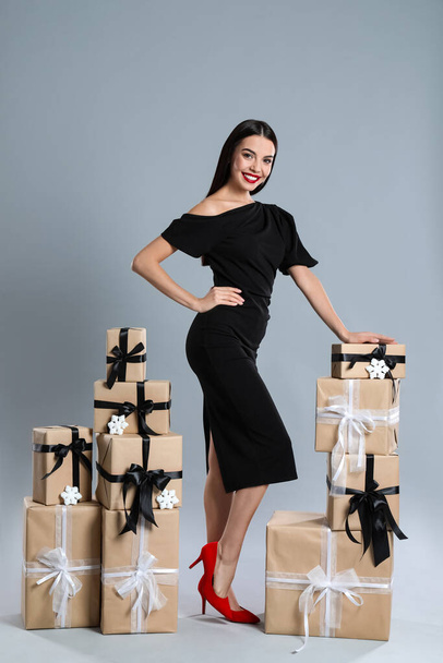 Woman in black dress with Christmas gifts on grey background - Fotografie, Obrázek