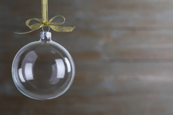 Transparent glass Christmas ball with golden ribbon and bow on blurred background. Space for text - Фото, зображення