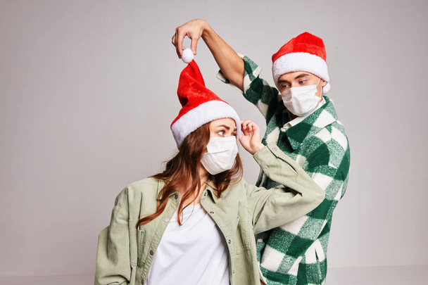 man en vrouw het dragen van santa hoeden kerstmis plezier medische maskers studio - Foto, afbeelding