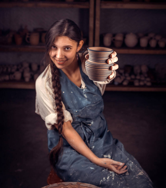 Ceramist meisje toont het afgewerkte klei product in kunststudio. Ambachten en ambachten. - Foto, afbeelding