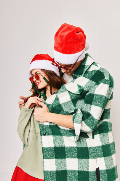 Um homem aquece uma mulher com uma camisa Chapéus de Natal feriado divertido óculos escuros - Foto, Imagem