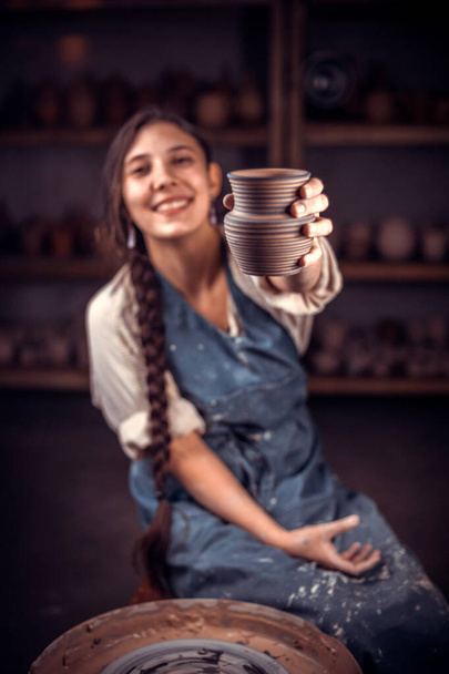 Elegante alfarero maestro mujer sentado en el banco con rueda de cerámica y haciendo olla de barro. Artesanía popular. - Foto, imagen