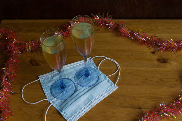 Concepto de Navidad y Año Nuevo con coronavirus. Copas de champán sobre una mesa de madera con máscaras covid19. Con decoración típica para fiestas de Nochevieja y trapo de cocina blanco con rayas rojas. - Foto, Imagen
