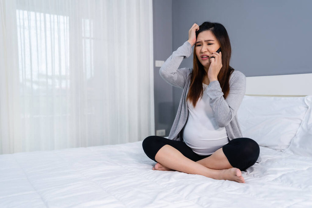 stressed pregnant woman talking on a mobile phone in a bed - Foto, afbeelding