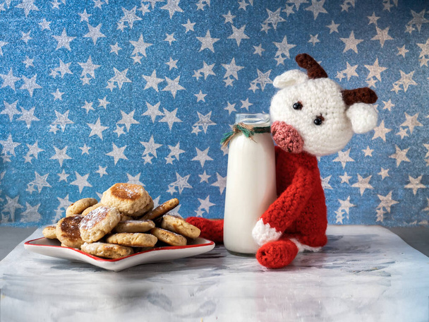 Śniadanie dla dzieci z dzianiną, byk w czerwonym swetrze i ciasteczka na świątecznym talerzu, mleko w szklanej butelce - Zdjęcie, obraz