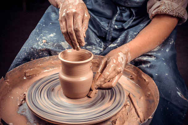 Master-ceramist creates a clay pot on a potters wheel. Hands of potter close up. Ancient craft and pottery handmade work - Photo, Image