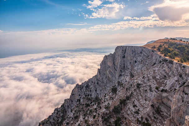 A majestic view of the rocky mountains and the valley in fog and clouds. Creamy fog covered the mountain valley in sunset light. Misty sunset over Crimea Mountains. Location place Ai-Petri, Crimea. - Foto, imagen