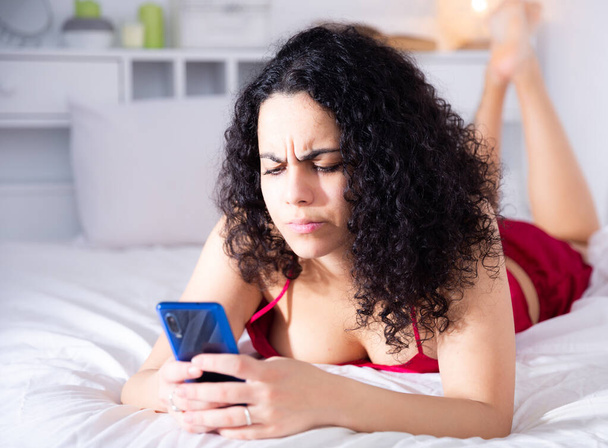 Dissatisfied woman using mobile phone in bed - Foto, Imagen