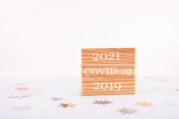 Ξύλινος κύβος με κείμενο 2021, Covid-19, 2019 σε φόντο επιτραπέζιου φωτισμού. Πρωτοχρονιάτικες έννοιες με πανδημία - Φωτογραφία, εικόνα