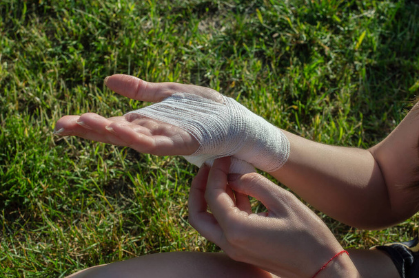 Młoda kobieta na zewnątrz podczas wędrówki niezależnie bandażuje uszkodzony nadgarstek. Widok z bliska - Zdjęcie, obraz