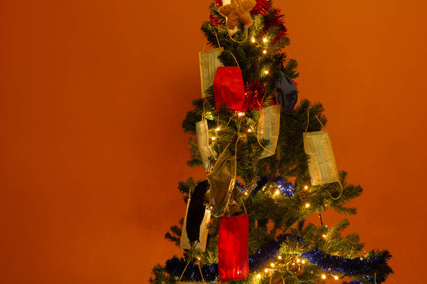 Рождественская елка украшена ковидом 19 маски на оранжевом фоне. Символический для другого Рождества. - Фото, изображение