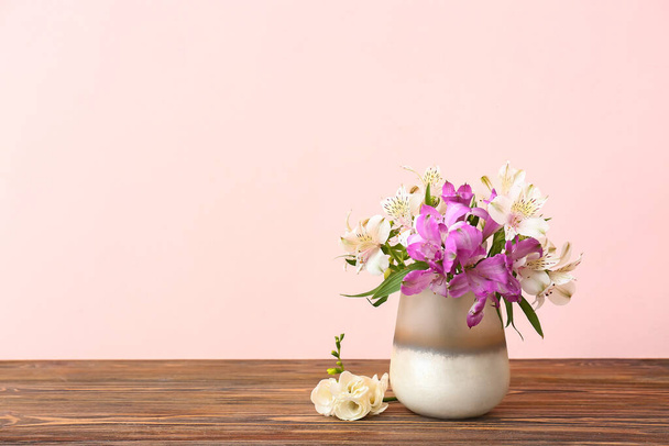 Beautiful vase with bouquet of flowers on wooden table against color background - 写真・画像