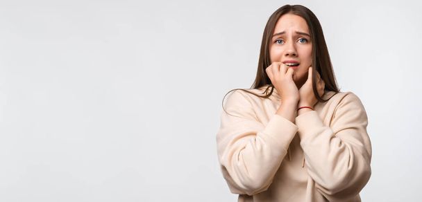 I'm afraid. Fright, phobia, panic attack, horror. Portrait of the scared woman with long chestnut hair, wearing stylish beige hoodie, isolated on white background. Copy space for your text - 写真・画像