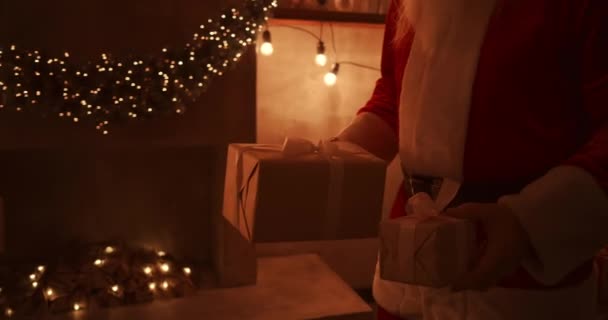 Κοντινό πλάνο του Άγιου Βασίλη: φέρνει δώρα κάτω από το χριστουγεννιάτικο δέντρο για τα παιδιά. Δώστε δώρα στα παιδιά τη νύχτα των Χριστουγέννων. Ο Άγιος Βασίλης βάζει ένα δώρο κάτω από το χριστουγεννιάτικο δέντρο - Πλάνα, βίντεο