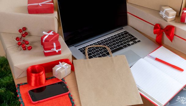 Laptop mit Geschenken, Kartons und Einkaufstasche am Arbeitsplatz, Lieferkonzept. - Foto, Bild