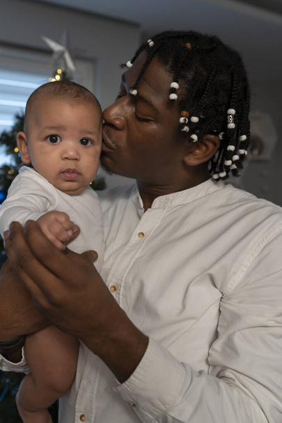 Afrika kökenli Amerikalı siyahi bir babanın melez bebeği tutarken portresi. Çok ırklı aile kavramı ve ilk bebek noeli - Fotoğraf, Görsel