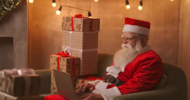 Santa Claus video calling tak to child on laptop hold present sit at home table. Pandemic and the isolation of the Santa congratulates children remotely - Footage, Video