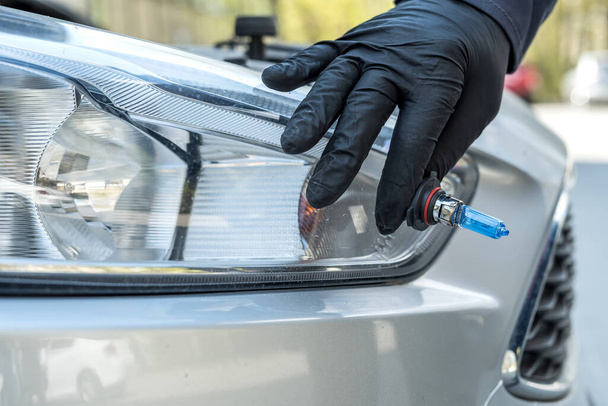 Mekaanikko vaihtamassa uutta halogeenilamppua auton ajovaloissa. autoteollisuus - Valokuva, kuva