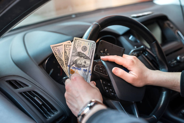 dólar y la llave del coche en la mano del hombre dentro del coche. pagar en bienes o alquilar coche - Foto, imagen