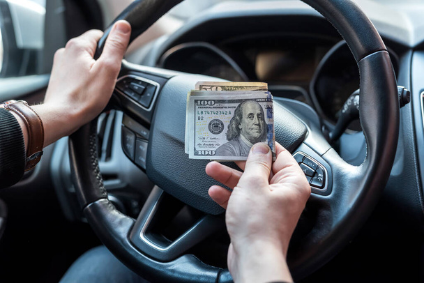 Hombre sosteniendo dólares sentado en el coche. comprar o alquilar, sobornar - Foto, imagen