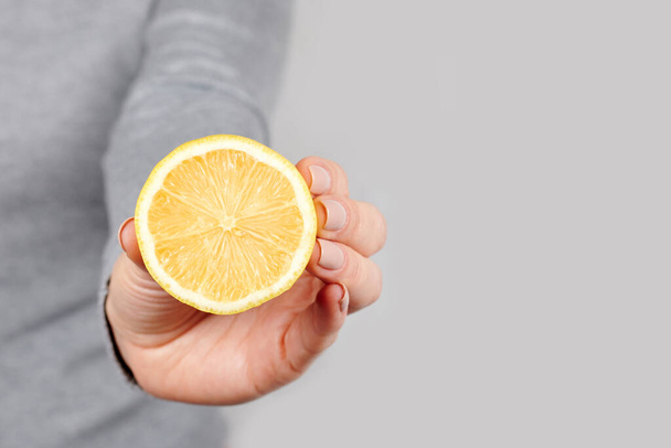 Hand with half lemon on grey. - Zdjęcie, obraz