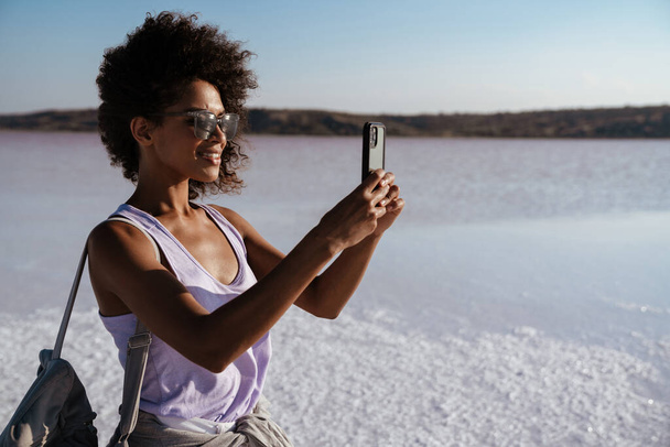 Image of happy african american woman taking photo on cellphone in salt valley - Fotó, kép