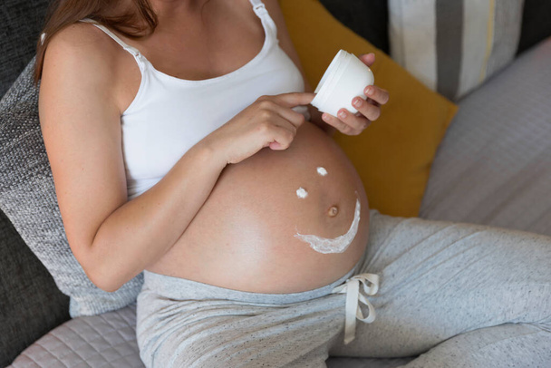 Pregnant woman applying stretch mark cream in her belly - Foto, imagen